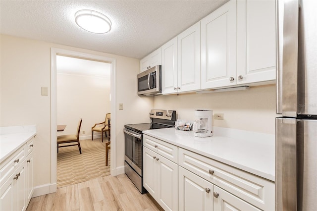 kitchen featuring white cabinets, light wood-style flooring, appliances with stainless steel finishes, light countertops, and a textured ceiling