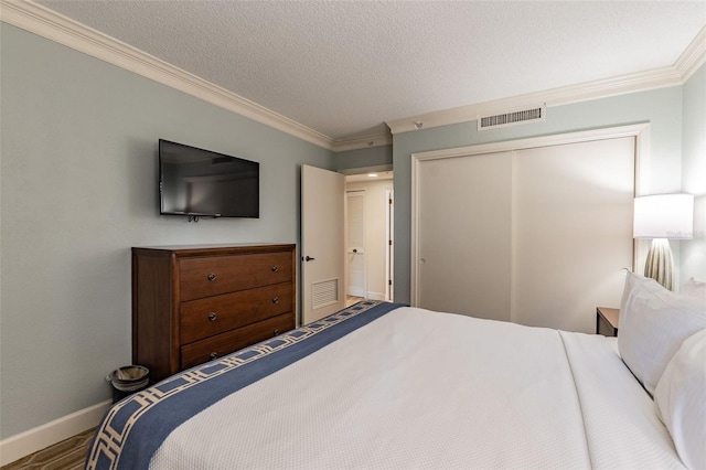 bedroom with a textured ceiling, visible vents, baseboards, ornamental molding, and a closet