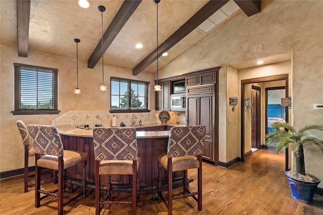 kitchen with light stone counters, hanging light fixtures, dark brown cabinets, and hardwood / wood-style floors