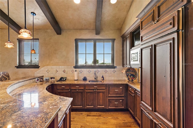 kitchen with dark wood-type flooring, built in appliances, sink, hanging light fixtures, and beam ceiling