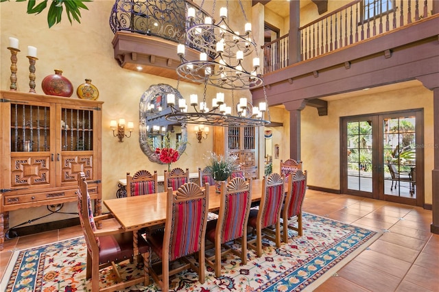 tiled dining room with a notable chandelier, a towering ceiling, french doors, and decorative columns