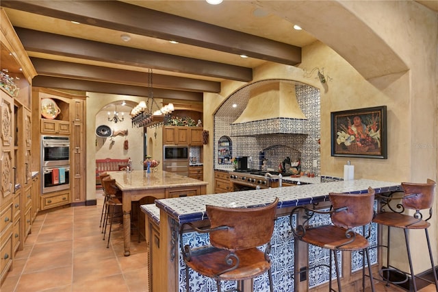 kitchen with a kitchen bar, kitchen peninsula, appliances with stainless steel finishes, a chandelier, and beam ceiling