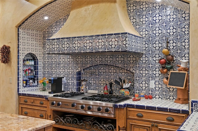 kitchen with premium range hood, backsplash, stainless steel gas stovetop, and tile countertops