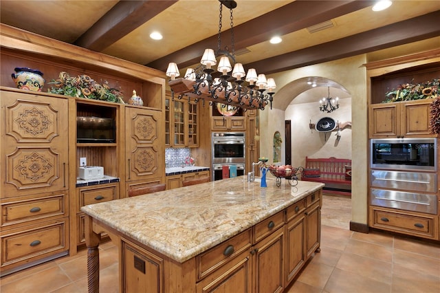 kitchen with decorative light fixtures, a kitchen island, beam ceiling, stainless steel double oven, and light stone counters