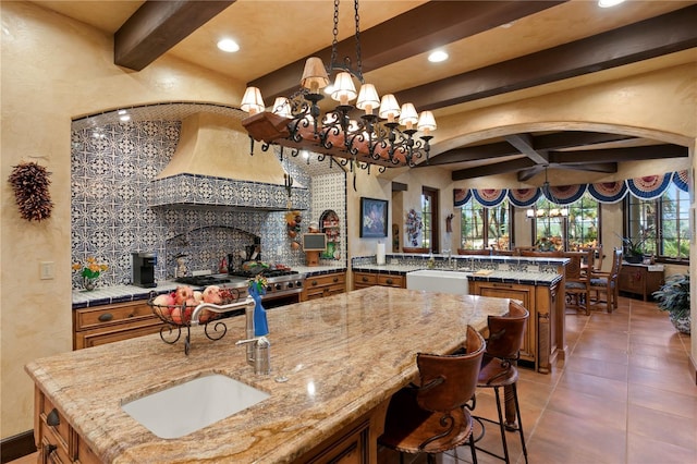 kitchen featuring backsplash, hanging light fixtures, kitchen peninsula, a center island with sink, and a breakfast bar area