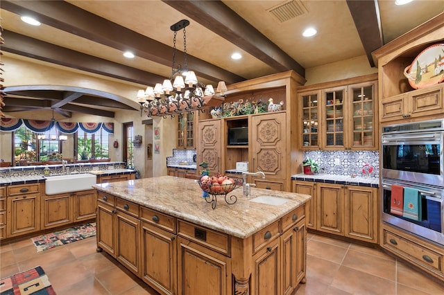 kitchen with a center island with sink, beam ceiling, sink, hanging light fixtures, and stainless steel double oven