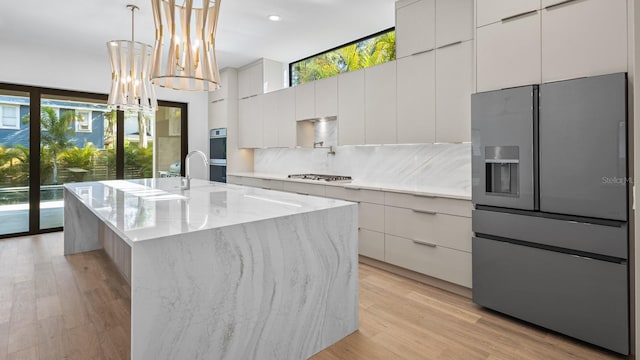 kitchen with decorative backsplash, appliances with stainless steel finishes, light wood-style floors, a kitchen island with sink, and modern cabinets