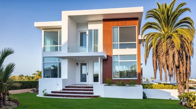 back of house with a balcony, a lawn, and stucco siding