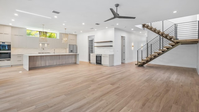 unfurnished living room with recessed lighting, beverage cooler, a ceiling fan, stairs, and light wood-type flooring