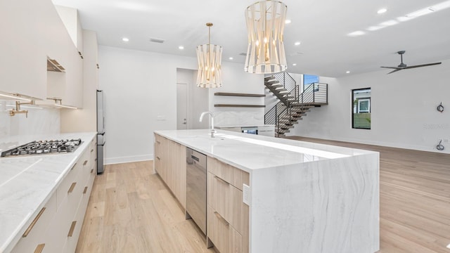 kitchen featuring stainless steel appliances, light wood-style flooring, light brown cabinets, a sink, and modern cabinets