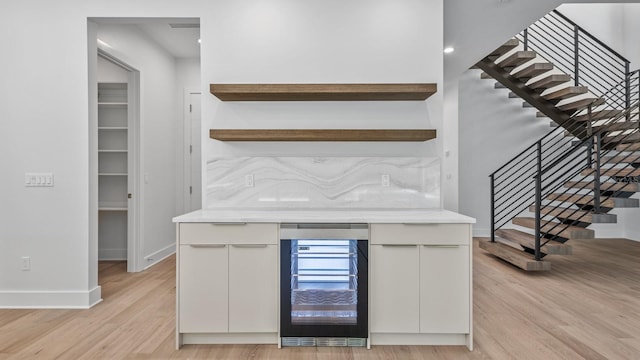 bar featuring stairs, wine cooler, baseboards, and light wood-style floors