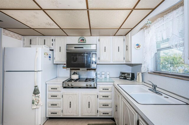 kitchen with a paneled ceiling, stainless steel gas stovetop, sink, white cabinets, and white fridge