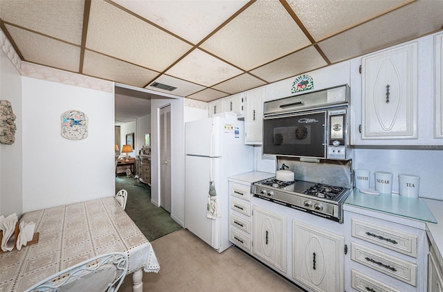 kitchen with white cabinetry, a drop ceiling, tile countertops, stainless steel gas stovetop, and white fridge