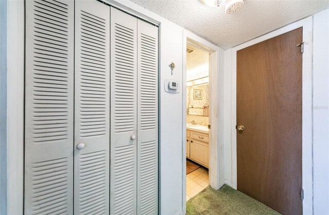 corridor with sink, light carpet, and a textured ceiling