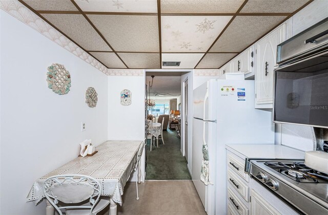 kitchen featuring a paneled ceiling, tile countertops, stainless steel gas cooktop, and white cabinets