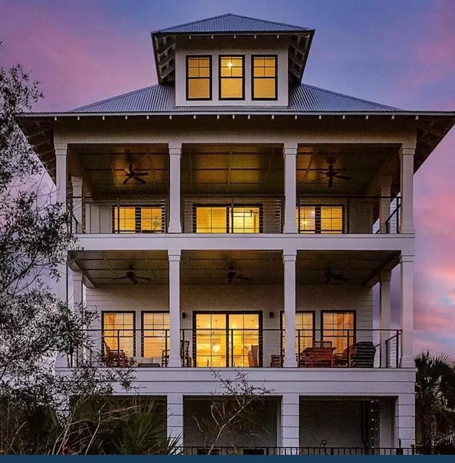 back house at dusk with ceiling fan and a balcony