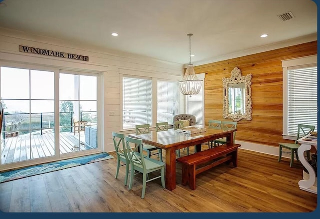 dining space with wood-type flooring, a notable chandelier, and wood walls