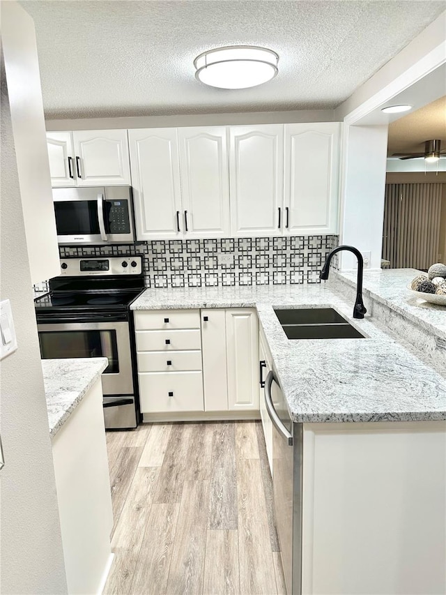 kitchen with sink, light stone counters, white cabinets, stainless steel appliances, and light wood-type flooring