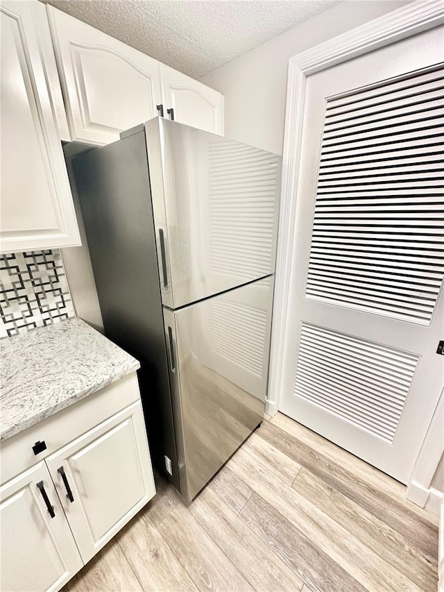 kitchen featuring white cabinetry, light stone counters, stainless steel fridge, and light hardwood / wood-style flooring