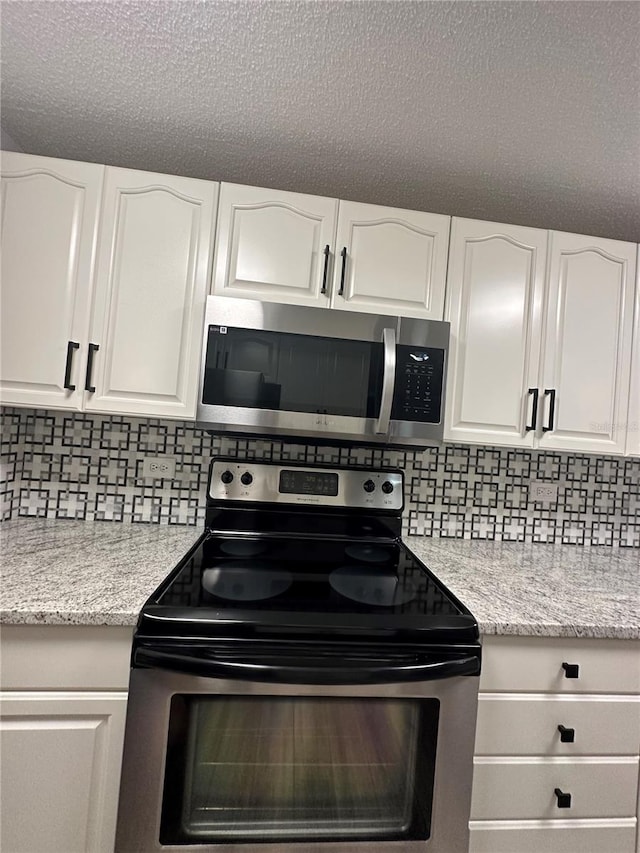 kitchen with a textured ceiling, tasteful backsplash, appliances with stainless steel finishes, and white cabinetry