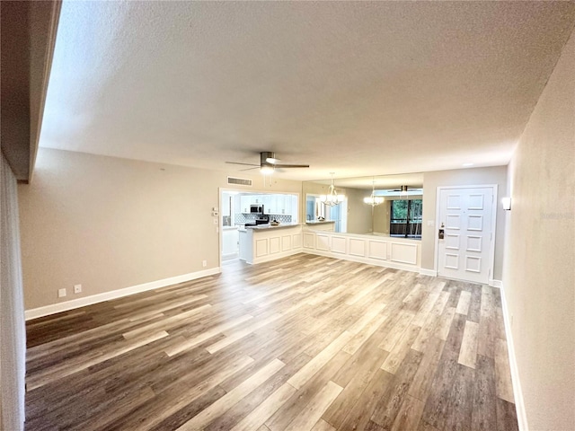 unfurnished living room with a textured ceiling, wood-type flooring, and ceiling fan with notable chandelier