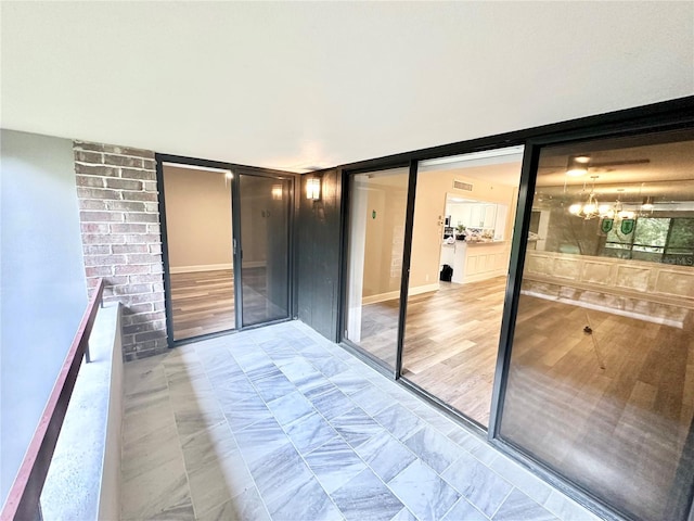 empty room with brick wall, a notable chandelier, and light hardwood / wood-style flooring