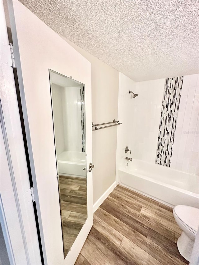 bathroom featuring tiled shower / bath, toilet, hardwood / wood-style flooring, and a textured ceiling