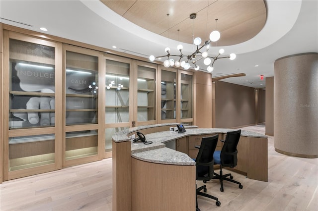 office area with an inviting chandelier, light hardwood / wood-style floors, and a raised ceiling