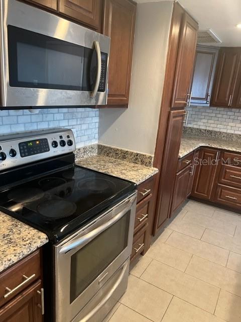 kitchen with backsplash, stainless steel appliances, light tile flooring, and light stone counters