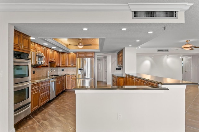 kitchen featuring tile patterned floors, a textured ceiling, a tray ceiling, kitchen peninsula, and stainless steel appliances