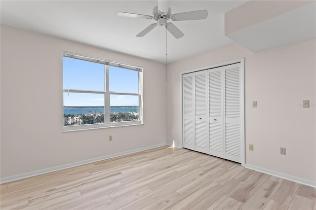 unfurnished bedroom featuring a closet, ceiling fan, light hardwood / wood-style flooring, and a water view