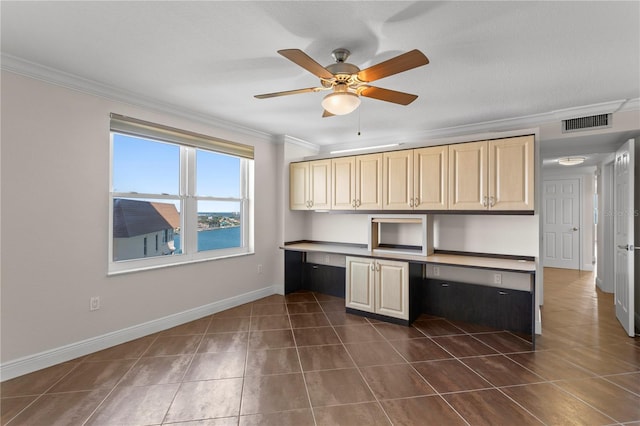 kitchen with ornamental molding, ceiling fan, cream cabinets, built in desk, and a water view