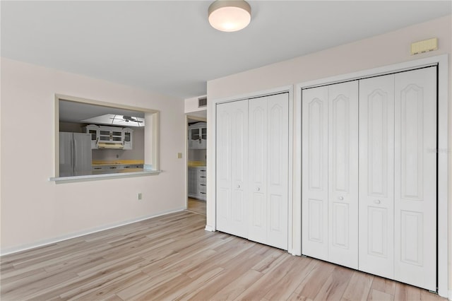 unfurnished bedroom with stainless steel refrigerator, multiple closets, and light wood-type flooring