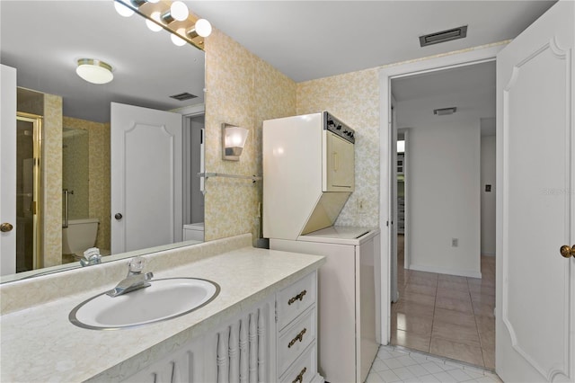 bathroom with walk in shower, tile patterned floors, toilet, vanity, and stacked washer and clothes dryer