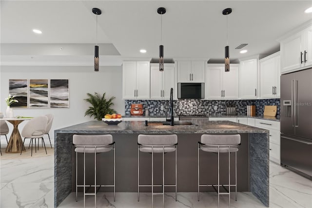 kitchen with an island with sink, a breakfast bar, stainless steel built in refrigerator, and white cabinetry