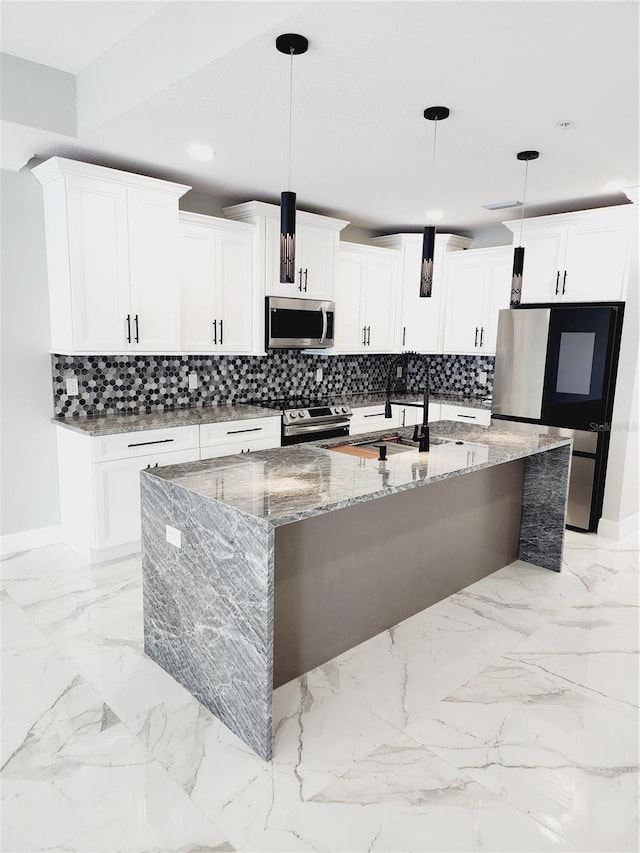 kitchen with light stone counters, pendant lighting, appliances with stainless steel finishes, and an island with sink