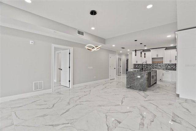 kitchen featuring sink, backsplash, pendant lighting, white cabinets, and a kitchen island with sink