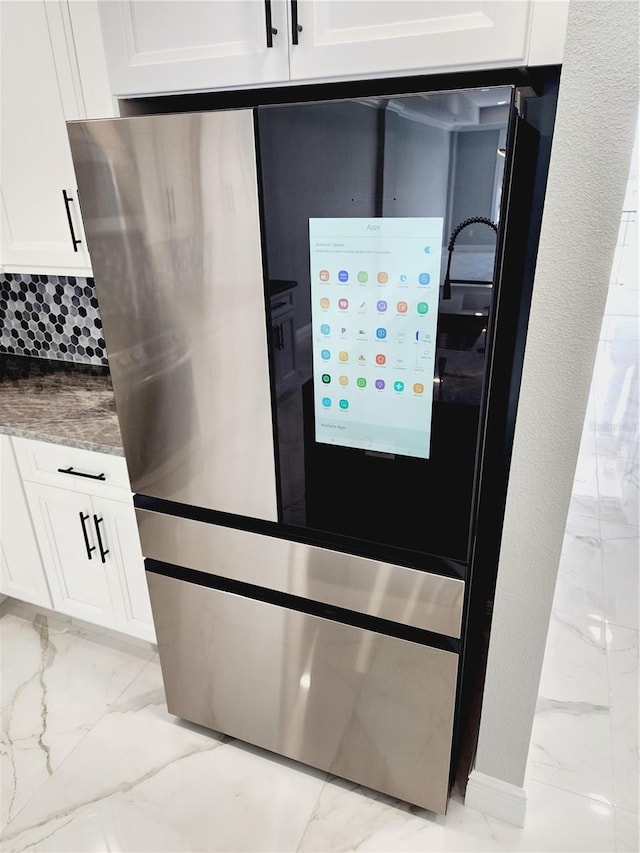 exterior details featuring decorative backsplash, white cabinetry, and stainless steel refrigerator