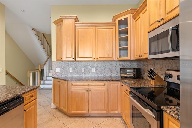 kitchen with tasteful backsplash, stainless steel appliances, light tile flooring, and dark stone counters