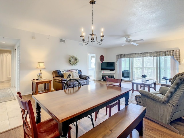 tiled dining area with a healthy amount of sunlight, a textured ceiling, and ceiling fan with notable chandelier