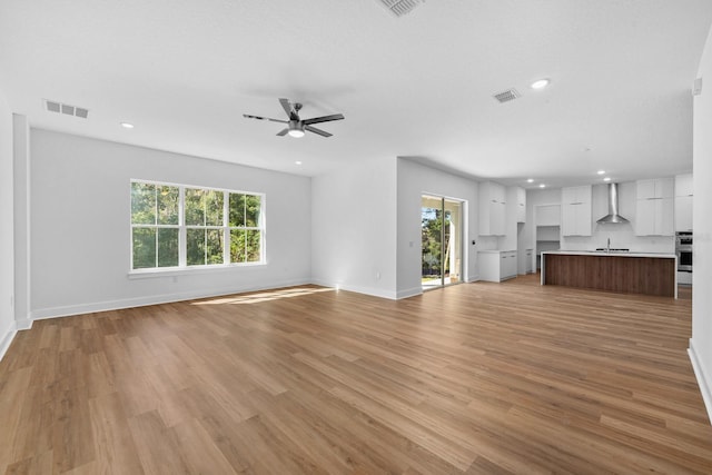 unfurnished living room featuring light hardwood / wood-style floors, ceiling fan, and sink