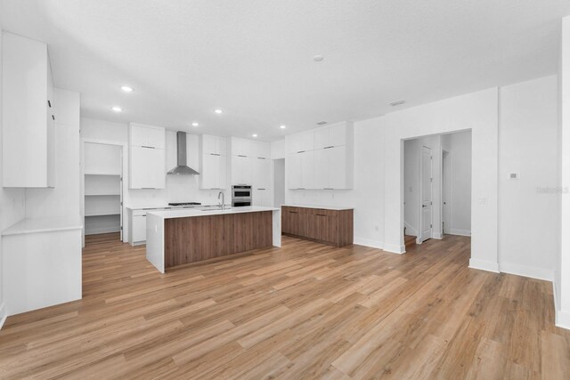 kitchen with light wood-type flooring, a spacious island, white cabinetry, and wall chimney exhaust hood