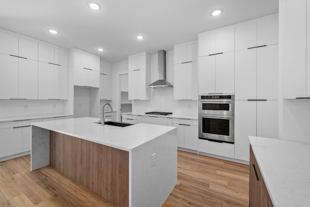 kitchen with white cabinets, appliances with stainless steel finishes, a center island with sink, and wall chimney exhaust hood