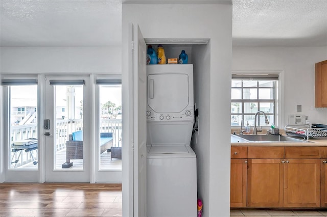 laundry room featuring stacked washer and clothes dryer, a textured ceiling, sink, and light wood-type flooring