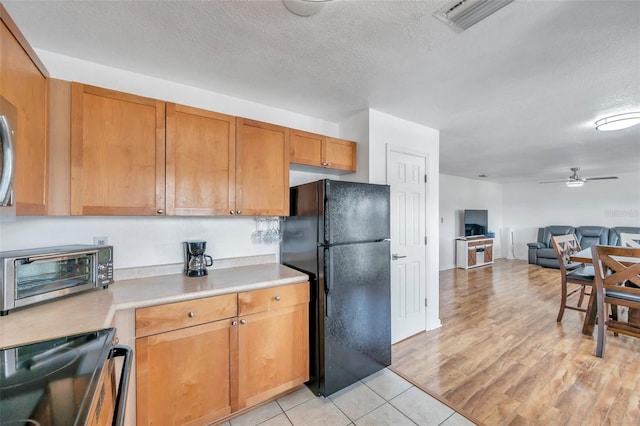 kitchen featuring light hardwood / wood-style floors, black refrigerator, ceiling fan, a textured ceiling, and range