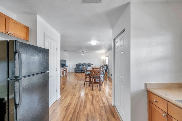 kitchen featuring a textured ceiling, ceiling fan, light wood-type flooring, and black fridge