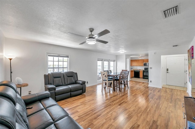 living room featuring a textured ceiling, ceiling fan, and light wood-type flooring