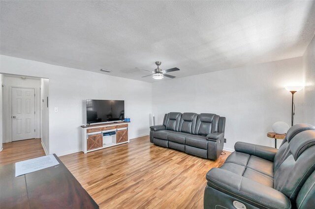 living room with light hardwood / wood-style floors, ceiling fan, and a textured ceiling