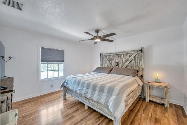 bedroom featuring a barn door, a textured ceiling, ceiling fan, and light wood-type flooring