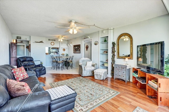 living room with built in features, hardwood / wood-style floors, a textured ceiling, and ceiling fan